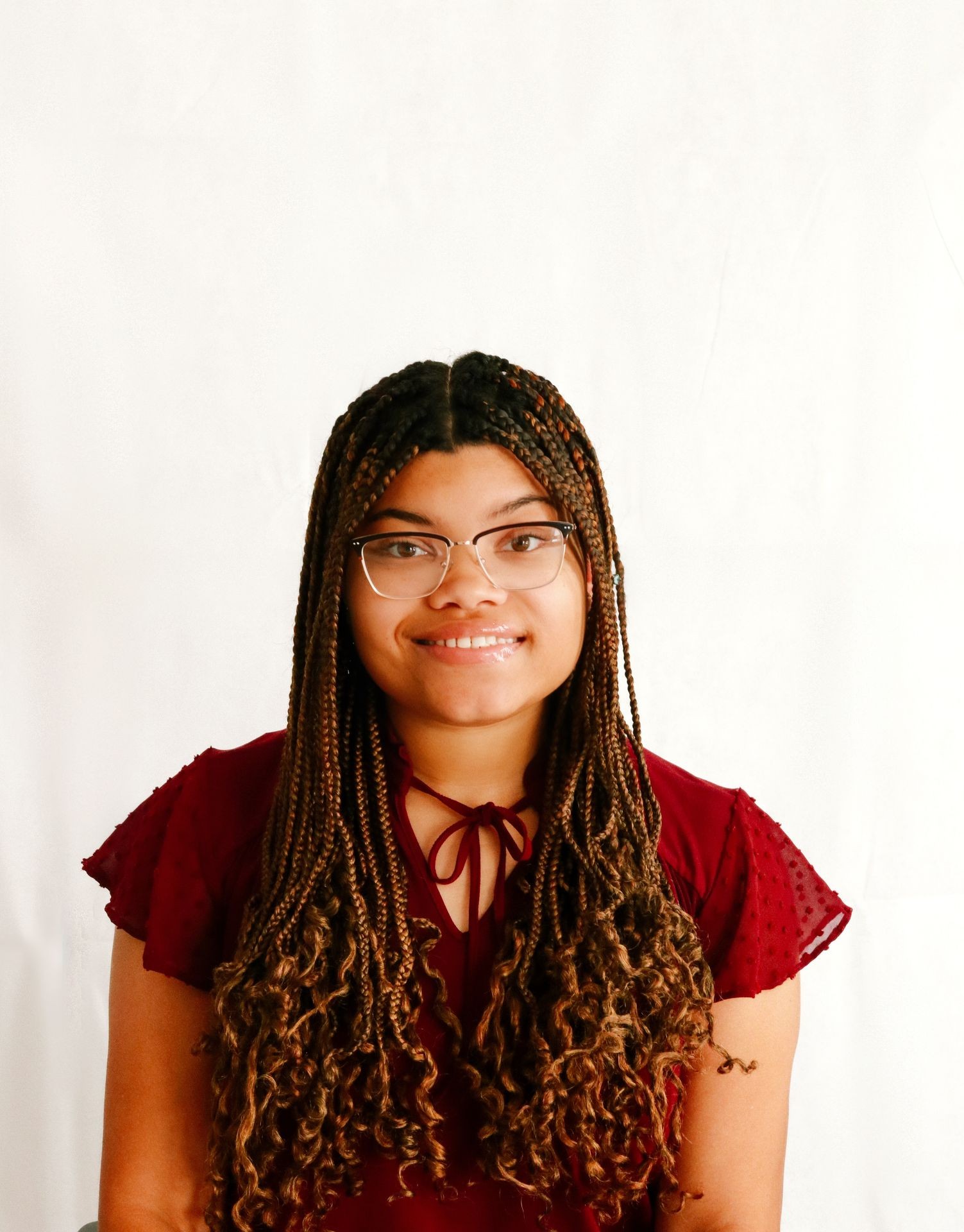 Person with braided hair wearing glasses and a burgundy blouse smiling against a plain white background.